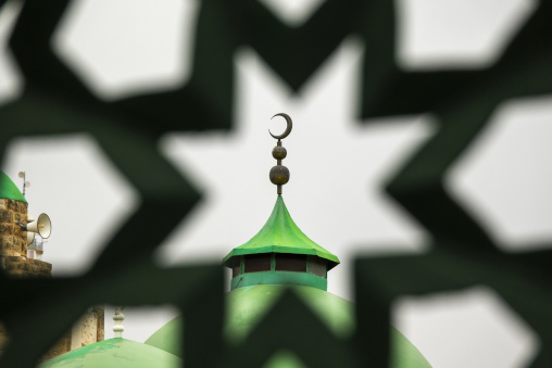 A green mosque dome topped with a crescent finial appears through a pierced star-patterned screen, North Governorate, Tripoli, Lebanon