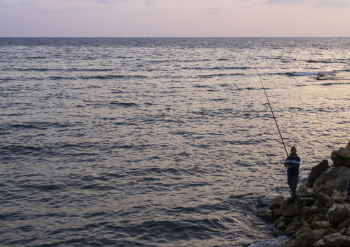 Man fishing at sunset from the seashore, North Governorate, Tripoli, Lebanon