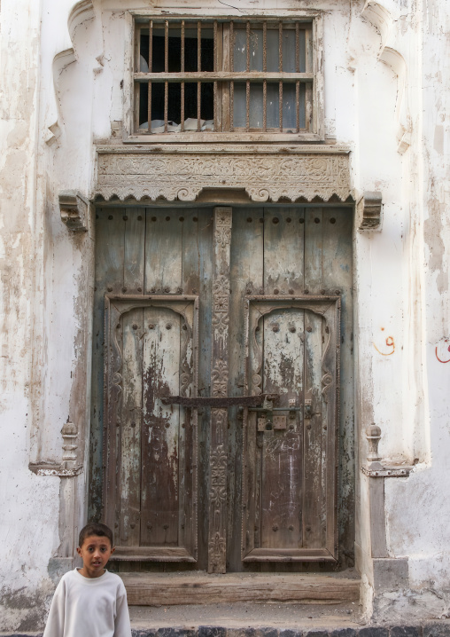 Yemeni boy in front of a wooden door of an old heritage house, Al Hudaydah Governorate, Hodeidah, Yemen