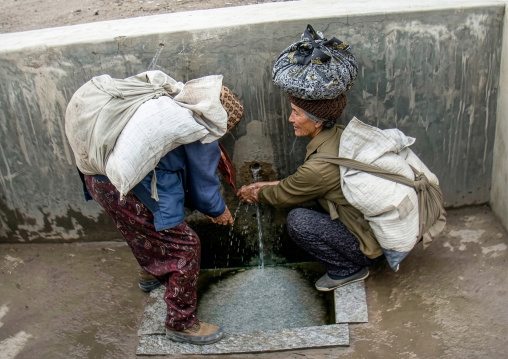 Women carrying heavy bags drinking water, South Pyongan Province, Chongsan-ri, North Korea