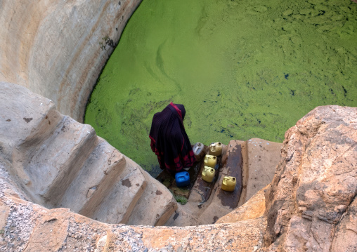 Woman collecting water in a green cistern, Amran Governorate, Shaharah, Yemen