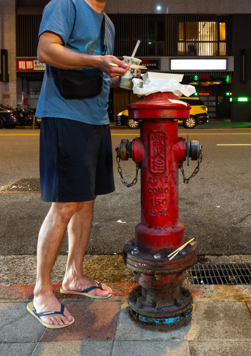 Man putting his food on a fire hydrant in Nanjichang night market, Zhongzheng District, Taipei, Taiwan