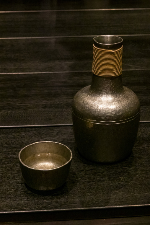 Traditional metal sake bottle and cup on a wooden table at Takef