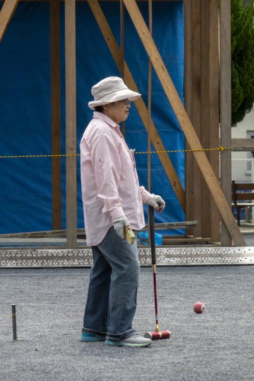 Elderly woman playing gateball with a mallet and ball in a park,