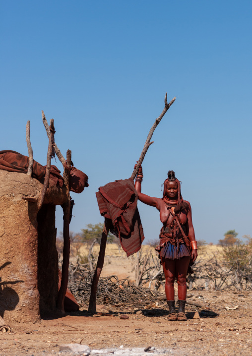Himba tribe woman standing in front of her mud hut, Cunene Province, Oncocua, Angola