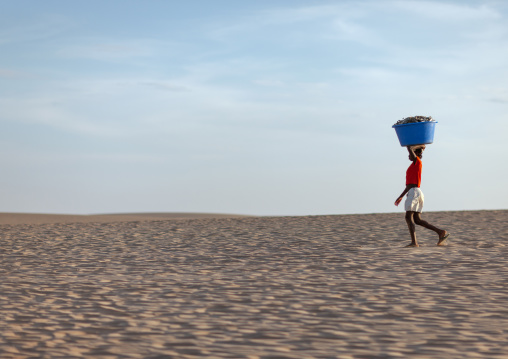 Angolan woman carrying fishes on her head along the beach, Namibe Province, Tombua, Angola