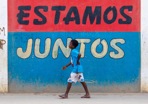 Angolan boy in front of a patriotic slogan on a wall, Benguela Province, Catumbela, Angola