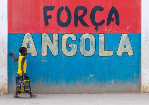 Angolan boy in front of a patriotic slogan on a wall, Benguela Province, Catumbela, Angola
