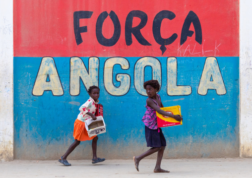Angolan girls in front of a patriotic slogan on a wall, Benguela Province, Catumbela, Angola