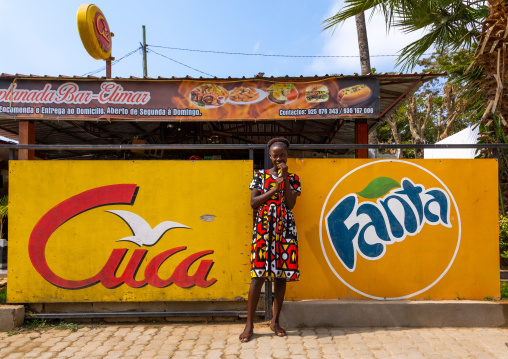 Angolan girl standing in front advertisement billboards, Benguela Province, Catumbela, Angola