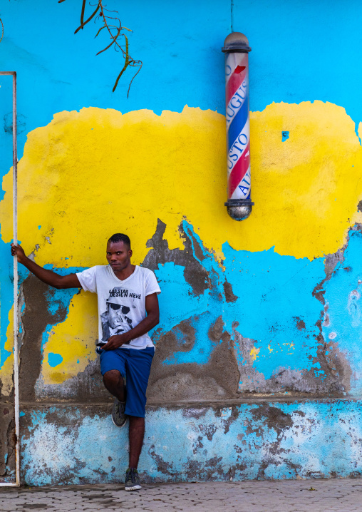 Angolan young man standing in front of a barber shop pole sign, Benguela Province, Benguela, Angola
