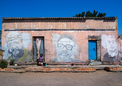 Woman in front of an old propaganda wall painting with Fidel Castro Jose Eduardo dos Santos and Leonid Brejnev, Cunene Province, Cahama, Angola