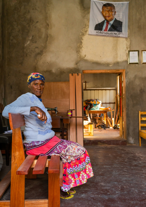 Angolan woman sit on a becnh inside her home under a portrait of joao lourenco, Namibe Province, Namibe, Angola