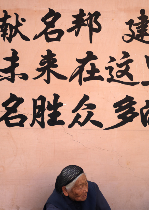 Old Woman In The Street Below Chinese Script On A Wall, Jianshui, Yunnan Province, China