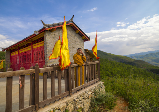 Monk Talking On Mobile Phone In Front Of Temple Over A Valley, Lijiang Area, Yunnan Province, China
