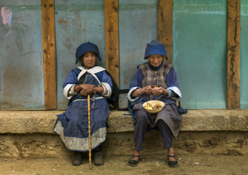 Naxi Minority Women Sit On A Bench, Lijiang, Yunnan Province, China
