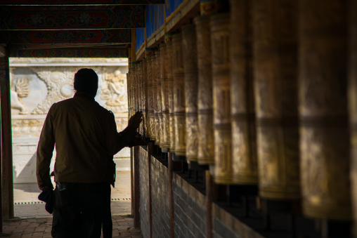 Tibetan pilgrim man turning prayer wheels in Shachong monastery, Qinghai Province, Wayaotai, China
