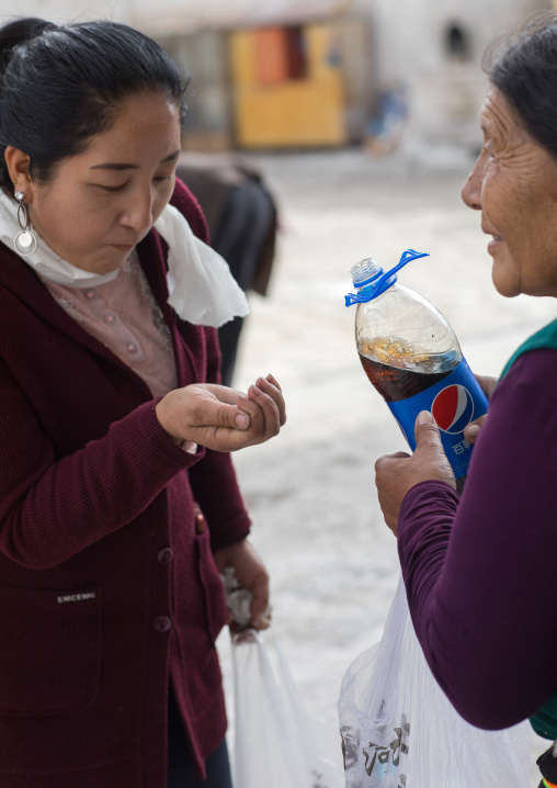 Tibetan woman drinking pepsi cola which has been blessed by the lamas in Rongwo monastery, Tongren County, Longwu, China