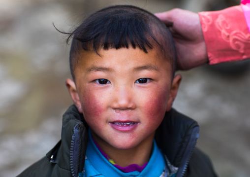 Portrait of a tibetan nomad child with his mother hand on his head, Qinghai province, Tsekhog, China