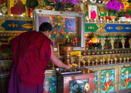 tibetan Monk lightening butter lamps inside Rongwo monastery, Tongren County, Longwu, China
