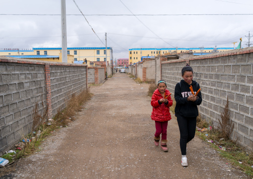 Tibetan children passing in front of houses build for nomads who are being forced off the land, Qinghai province, Sogzong, China