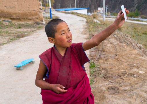 Young tibetan monk holding a polaroid in his hand in Lhachub monastery, Gansu province, Lhachub, China