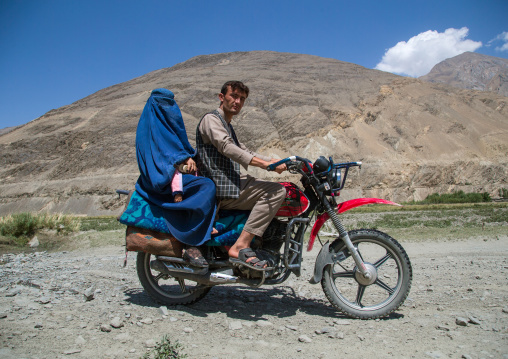 Afghan man riding a motorcycle with his wife wearing a burka, Badakhshan province, Qazi deh, Afghanistan
