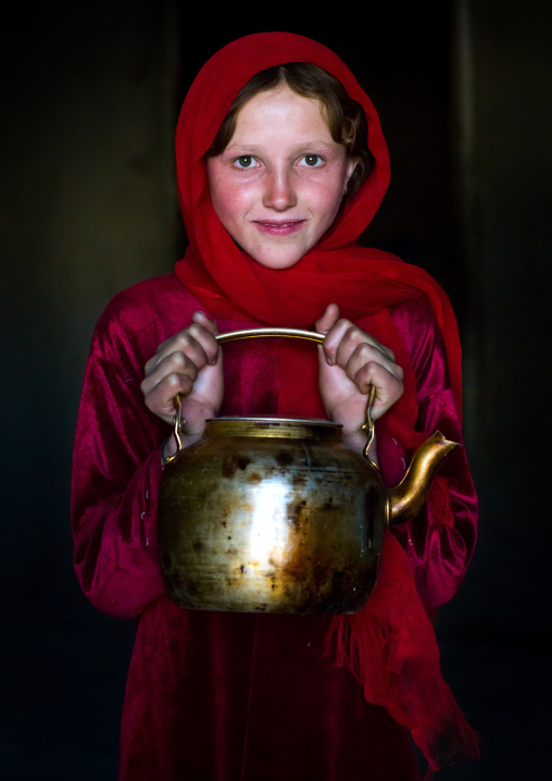 Portrait of an afghan girl with pale skin wearing red clothes and holding a tea pot, Badakhshan province, Khandood, Afghanistan
