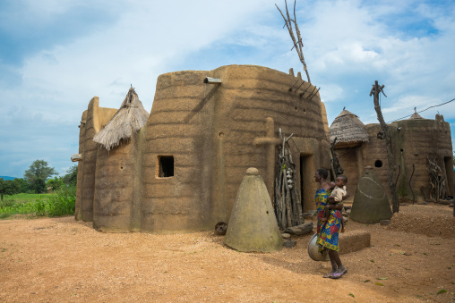 Benin, West Africa, Boukoumbé, mother and her baby in front of her traditional tata somba house with thatched roofs and granaries