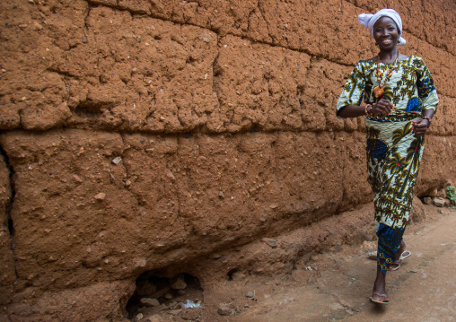 Benin, West Africa, Savalou, woman walking quickly along an adobe wall