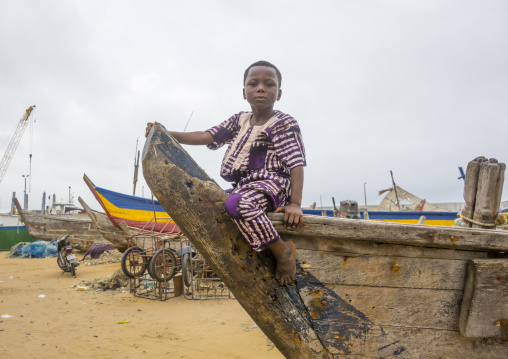 Benin, West Africa, Cotonou, boy sit on a fishermen boat in the port