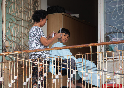 A boy having his hair cut by his mother on a balcony, Phnom Penh province, Phnom Penh, Cambodia