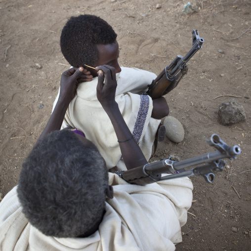 Karrayyu Tribe Man Squatting With His Kalashnikov While Having His Gunfura Hairstyle Done During Gadaaa Ceremony, Metahara, Ethiopia