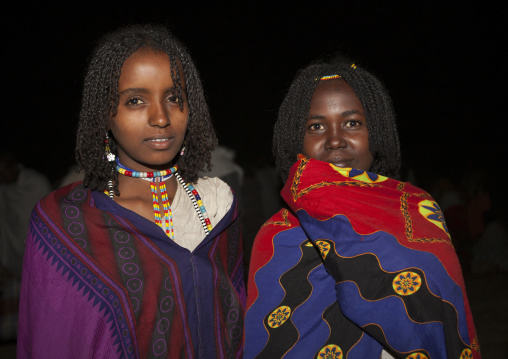 Night Shot Of Two Smiling Karrayyu Tribe Girls With Stranded Hair, Colourful Wrap Around Clothes And Colourful Necklaces During Gadaaa Ceremony, Metahara, Ethiopia