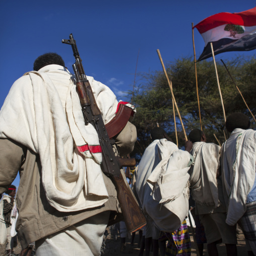 Rear View Of A Karrayyu Tribe Man Carrying A Kalashnikov Passing By A Group Of Karrayyu People With Oromo Flag People During Gadaaa Ceremony, Metahara, Ethiopia