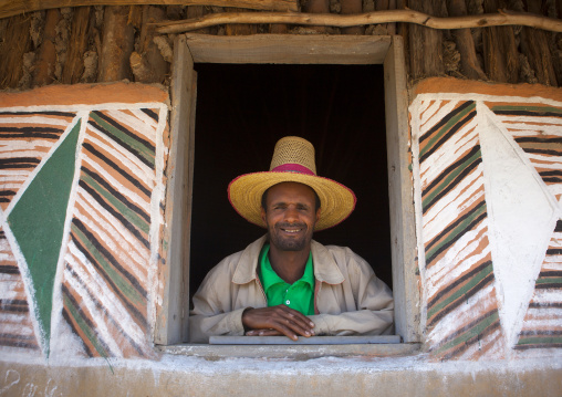 Portrait of a muslim man with tall hat standing at the window of his painted tukul, Alaba, Ethiopia