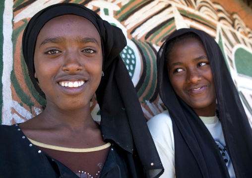 Portrait of muslim Ethiopian girls with toothy smiles and black veils outside a painted tukul, Alaba, Ethiopia
