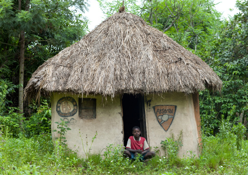 Concrete house with thatch roof ari teenage boy squatting omo valley Ethiopia