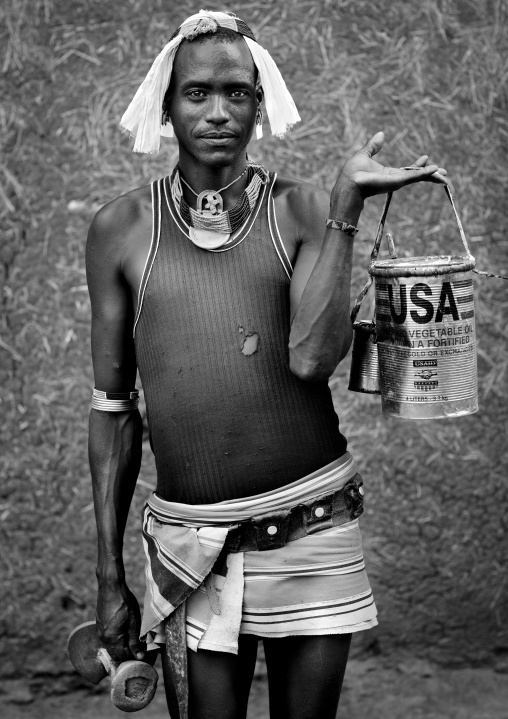 Fashionable tsemay tribe man posing with a can and carrying a headrest in key afer, Omo valley, Ethiopia