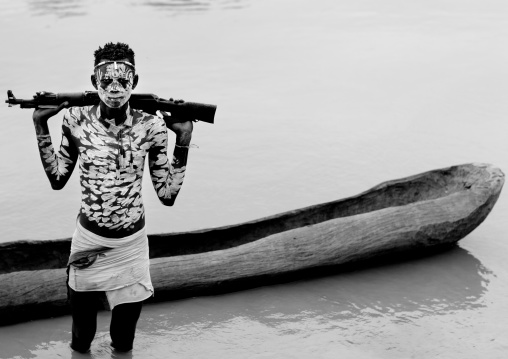 Young Karo Man With White Painted Faces And Chests Holding Kalashnikov Rifle In The Water Of The River  Near Pirogue Omo Valley Ethiopia