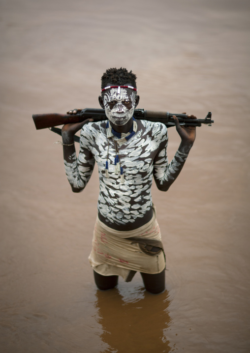 Young Karo Man With White Painted Faces And Chests Holding Kalashnikov Rifle In The Water Of The River Omo Valley Ethiopia