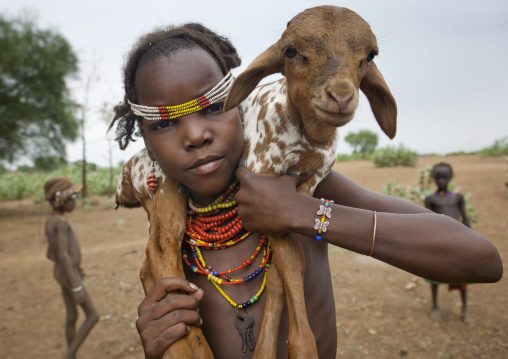 Young Dassanech Girl With Beaded Headband Carries A Baby Goat On Shoulders Omorate Ethiopia