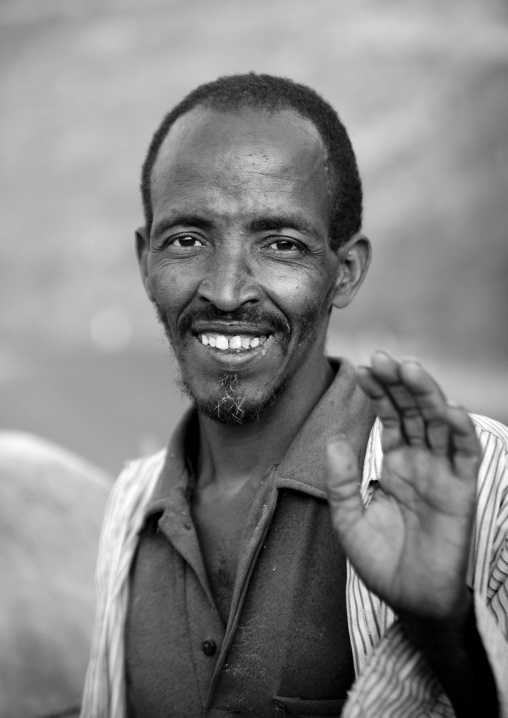 Black and white portrait of a man with toothy smile waving at camera, Dire dawa, Ethiopia
