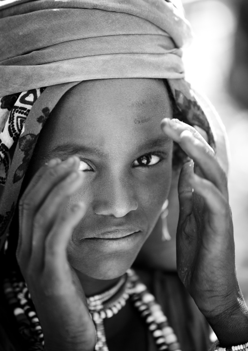 Black And White Portrait Of A Shy Karrayyu Tribe Girl With Jewels And Head Scarf Putting Her Hand Around Her Face, Metehara, Ethiopia