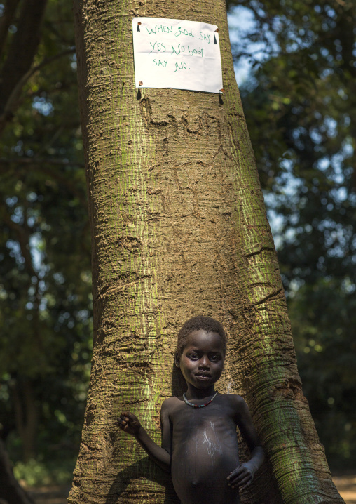 Anuak Tribe Child In Front Of A Tree With A Bible Sentence On It, Gambela, Ethiopia