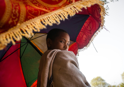 Boy holding an umbrella during kidane mehret orthodox celebration, Amhara region, Lalibela, Ethiopia