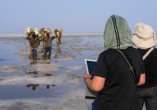 Tourists taking pictures of a camel caravan carrying salt through the danakil depression, Afar region, Dallol, Ethiopia