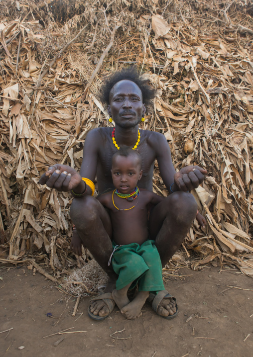 Dassanech tribe father and son sit in front of their house, Omo valley, Omorate, Ethiopia