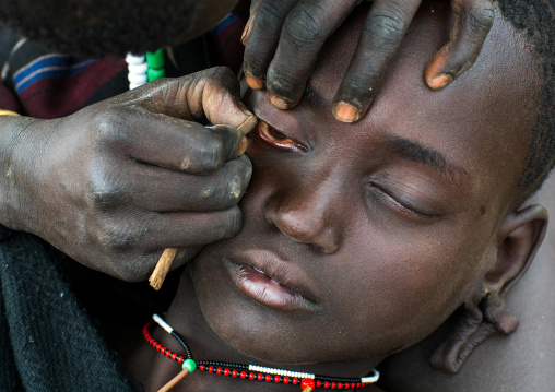 Mursi tribe woman removing the eyelashes of her friend, Omo valley, Mago park, Ethiopia