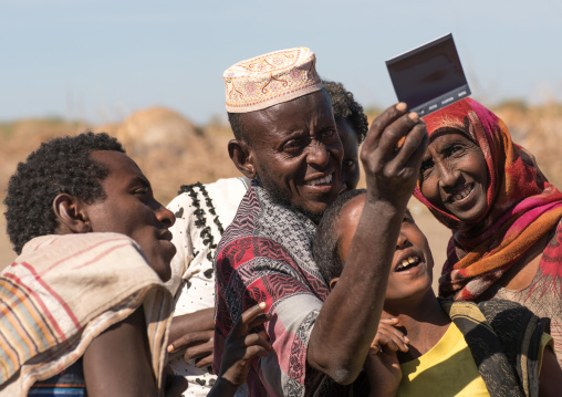 Afar tribe people looking polaroid pictures of themselves, Afar region, Assayta, Ethiopia